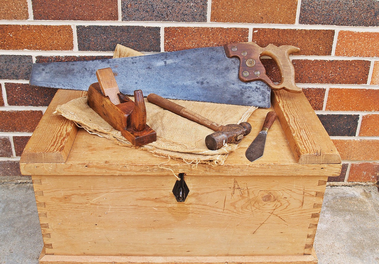 A carpenter's wooden toolbox against a brick wall, hand saw and plane poking out the top